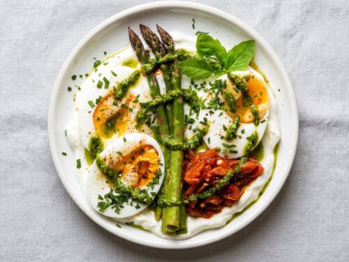 proteinrik frokost servert på hvit tallerken med kokt egg, yoghurt, asparges og pesto
